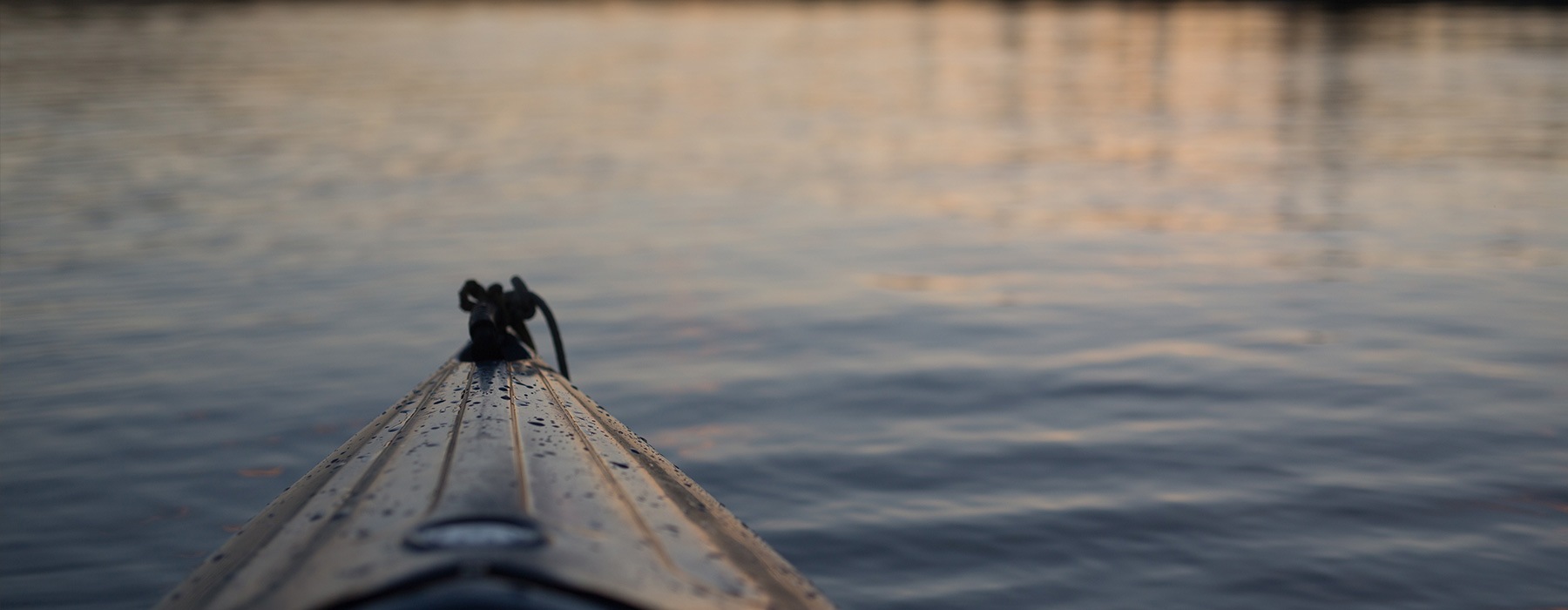 lifestyle image of the end of a rowboat on reflective water